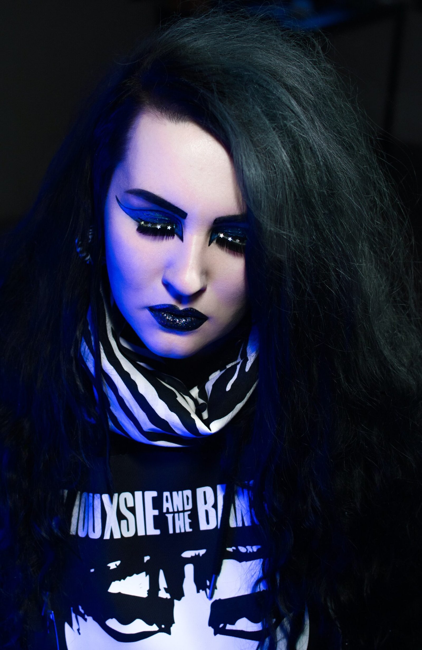 Close-up of goth woman with black glitter lipstick, bold eyeliner, and dramatic starry eyelashes.