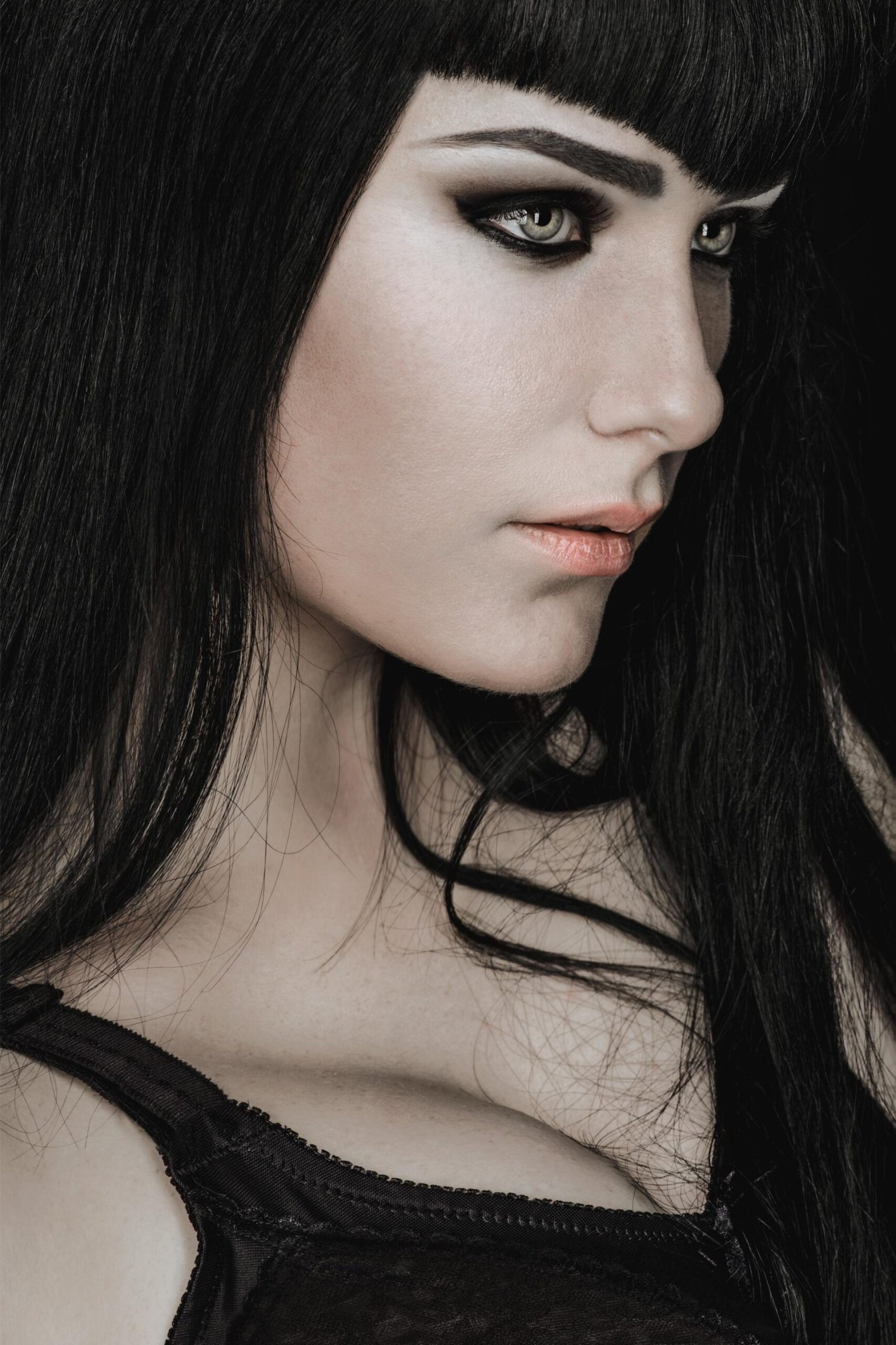 Close-up of gothic woman's face with smoky eye makeup and long black hair.
