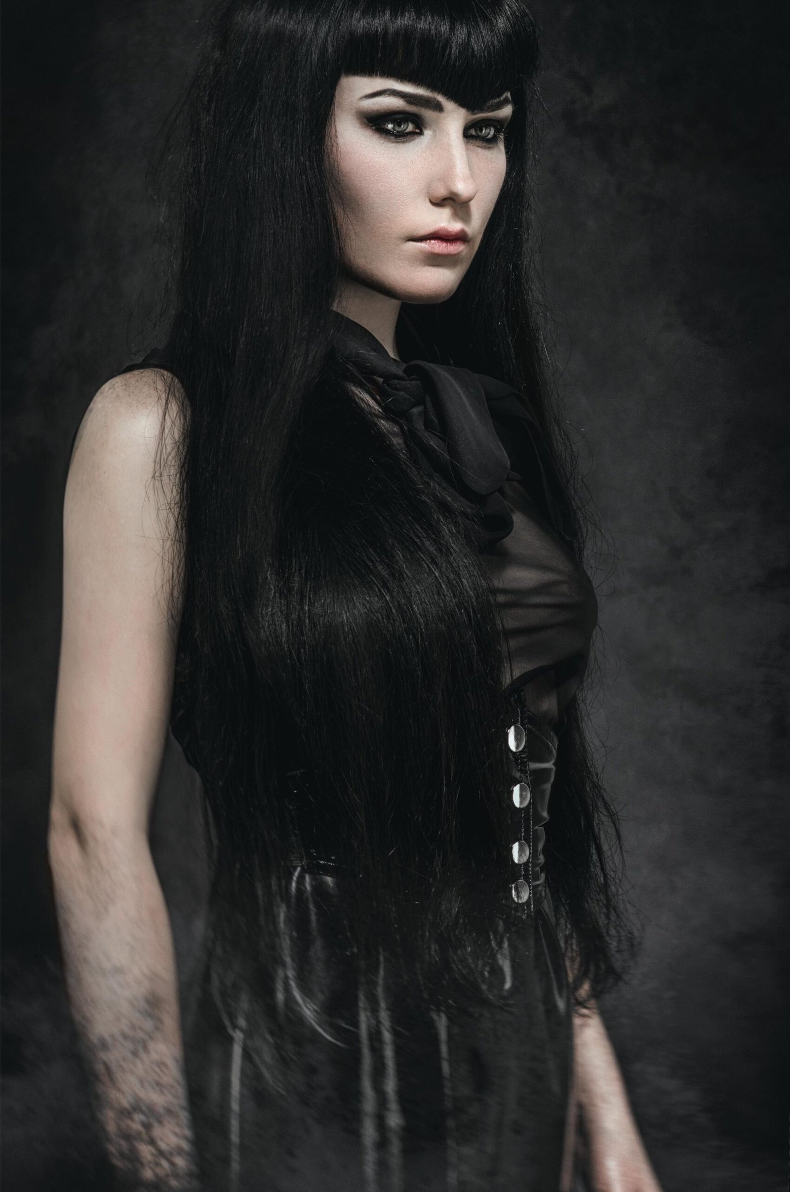 Gothic woman in black corset top and long hair, moody portrait with intense gaze.