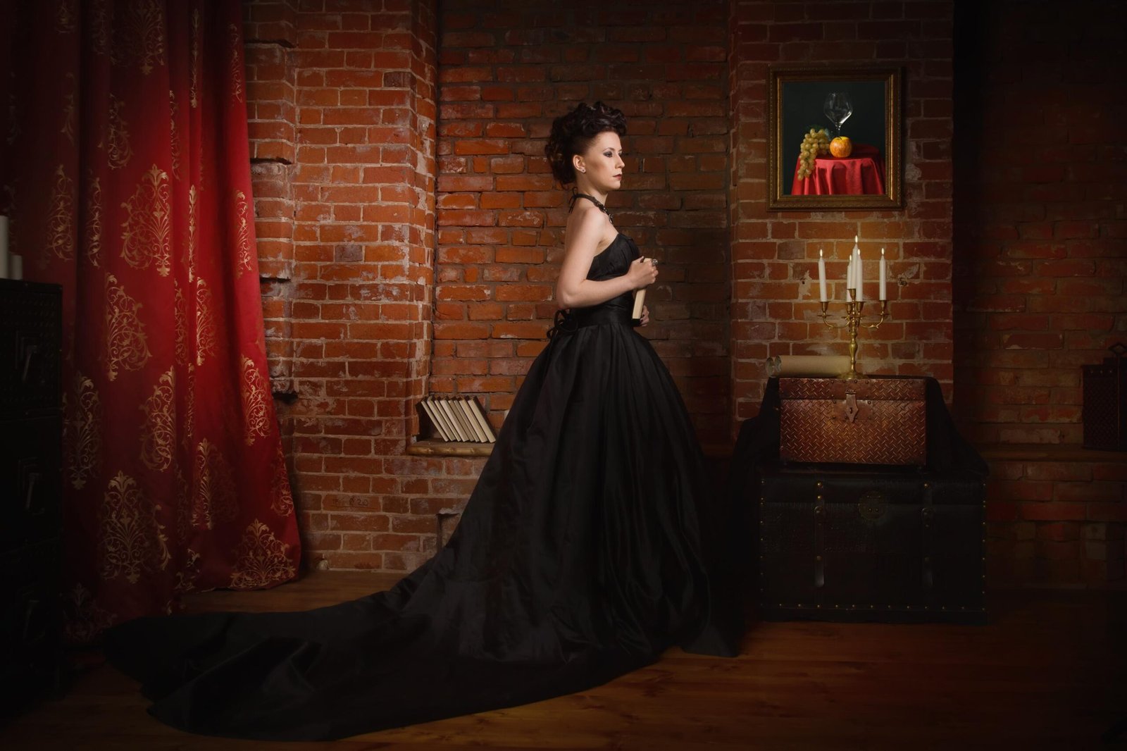 Woman in full-length black ball gown standing in gothic Victorian interior.
