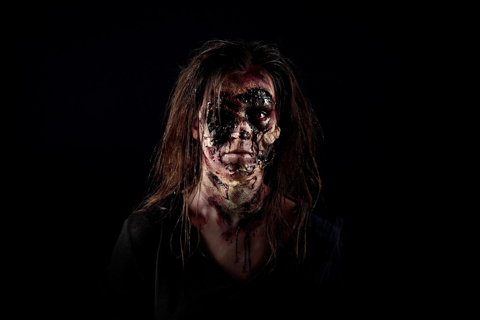 Horror-style woman with melted face makeup and long hair staring into darkness with haunting expression.