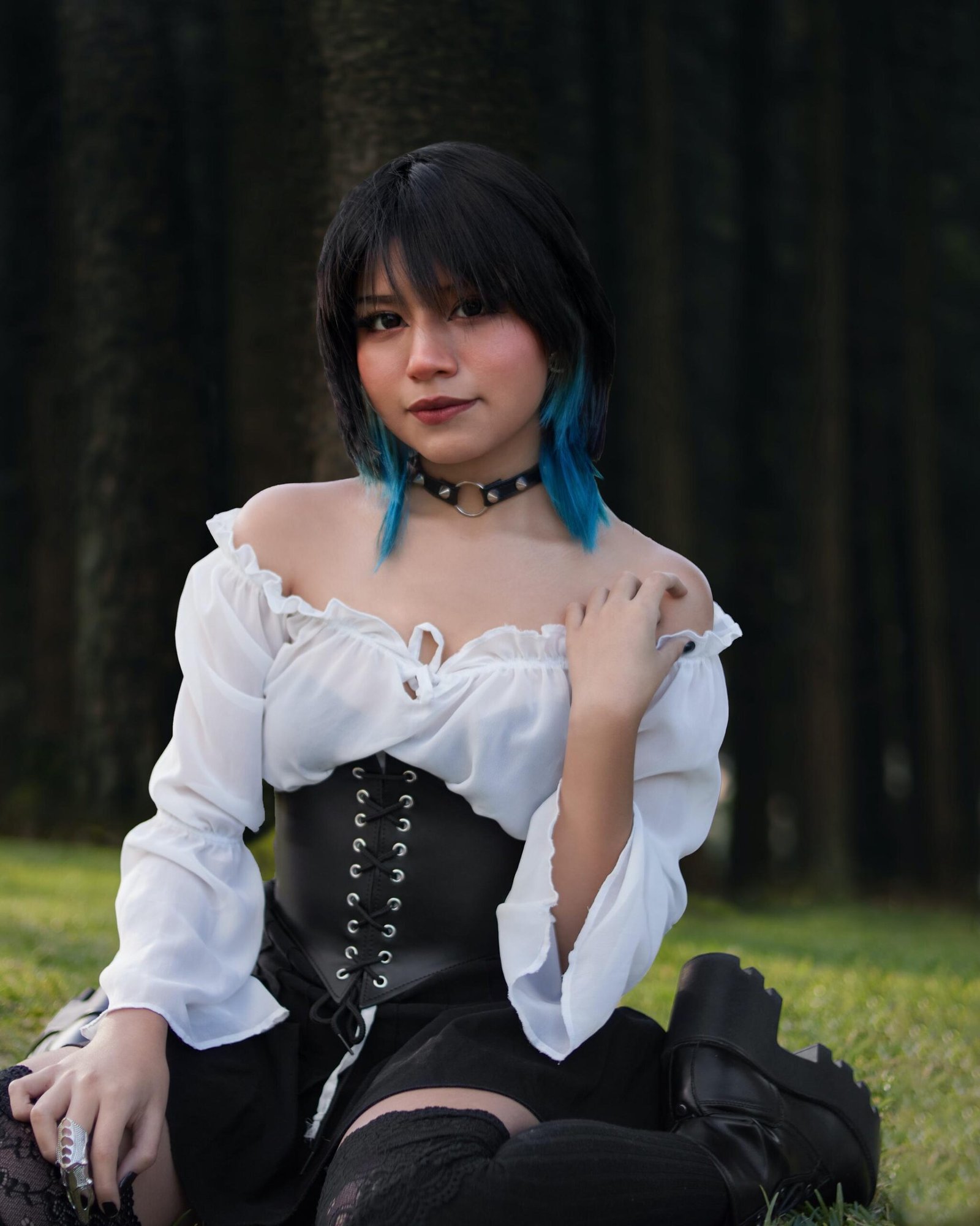 Woman with short dark hair, white blouse and corset sitting on grass, gothic choker necklace