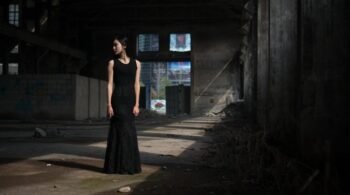 Full view of woman in long black lace gothic skirt standing in abandoned warehouse