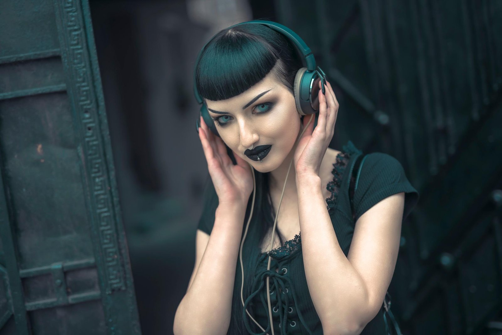 Gothic woman with black lipstick and headphones, piercing gaze while standing outdoors.