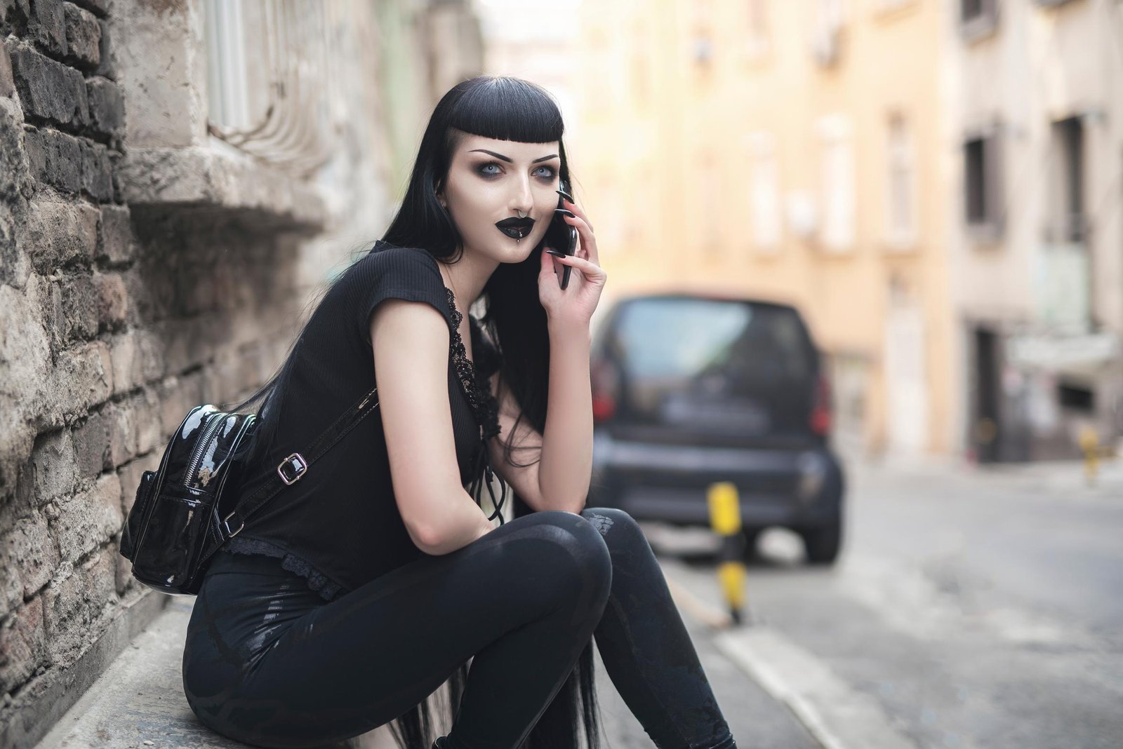 Goth woman with black lipstick sitting on a street curb, holding a phone