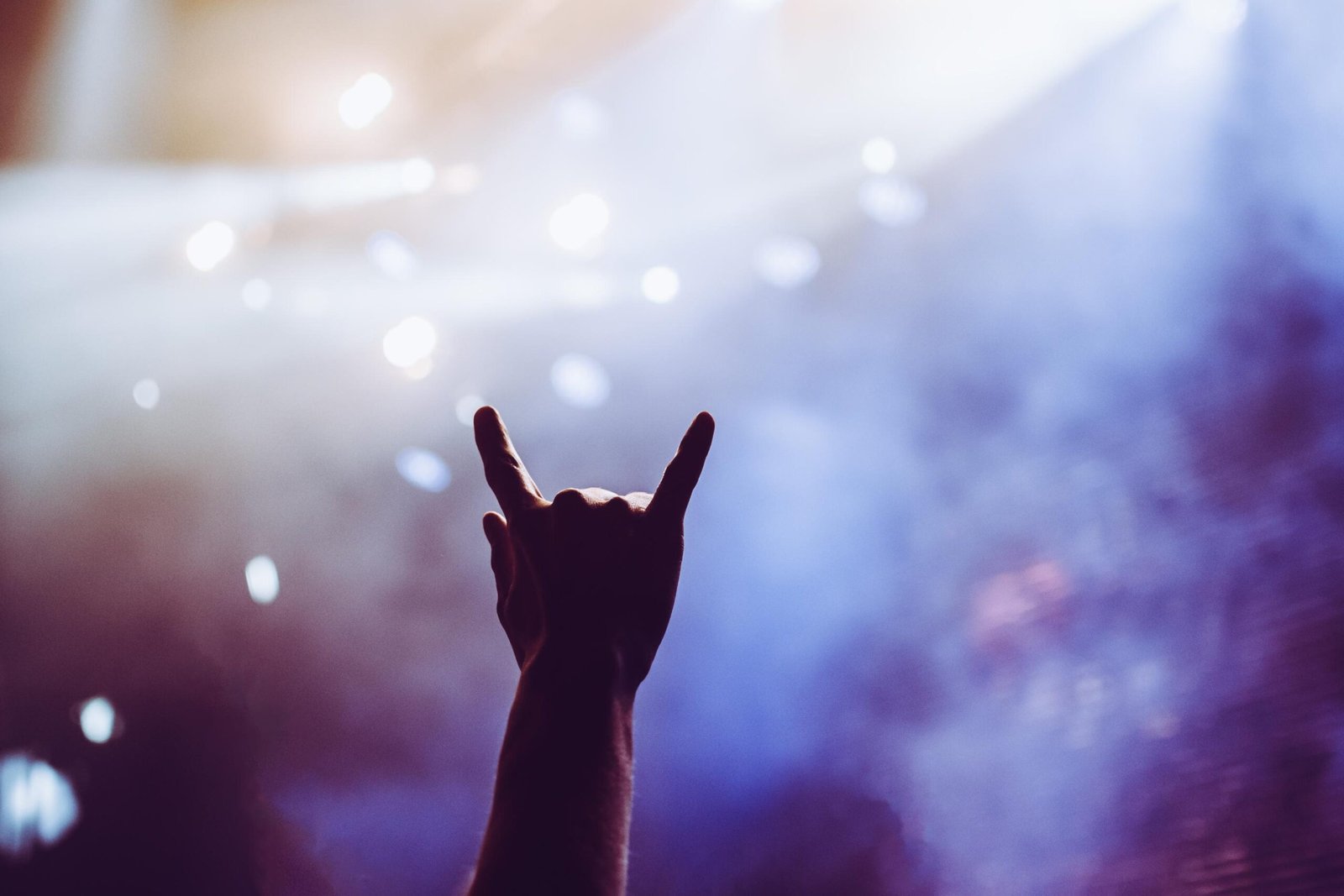 Raised hand showing metal horns at a live concert under stage lights