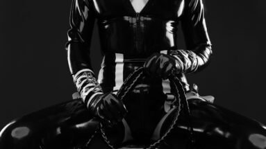 Woman in black latex catsuit and mask lying on floor, covered in spilled liquid.