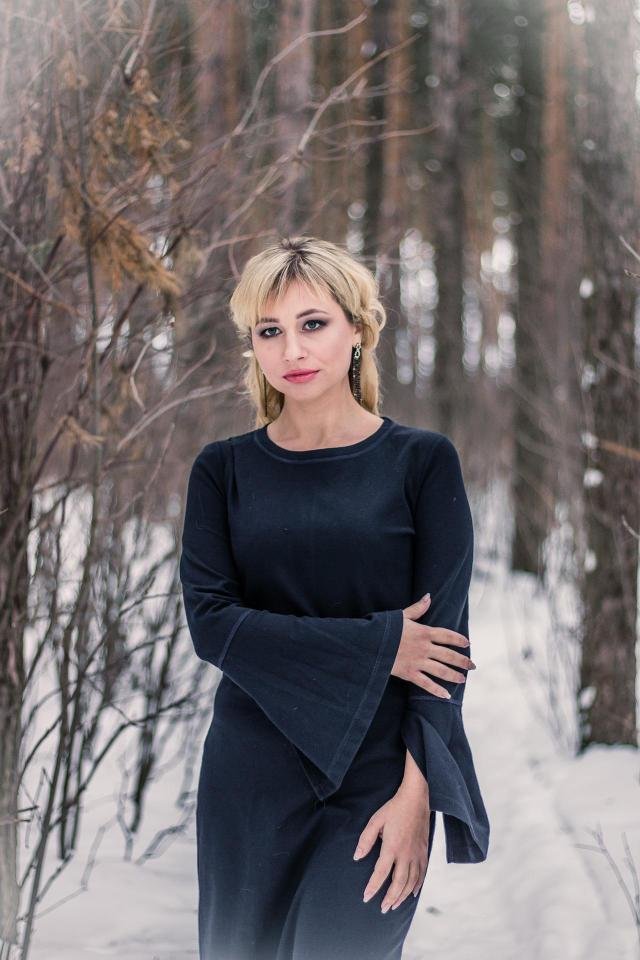 Woman in black dress looking upward in snowy forest, dramatic gothic winter portrait