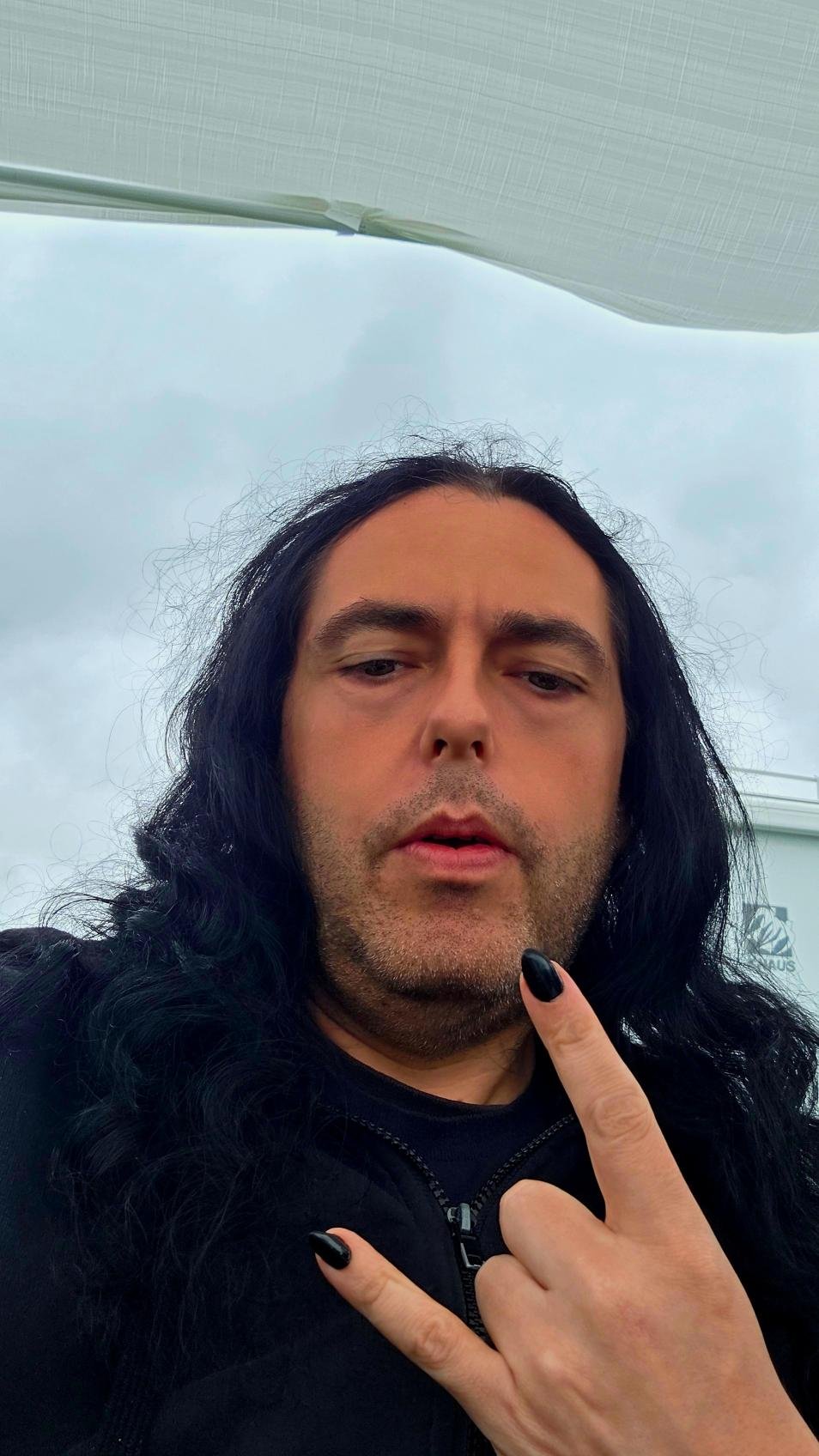 Xavi at Wacken Open Air 2025, holding up metal horns with black nail polish under grey sky