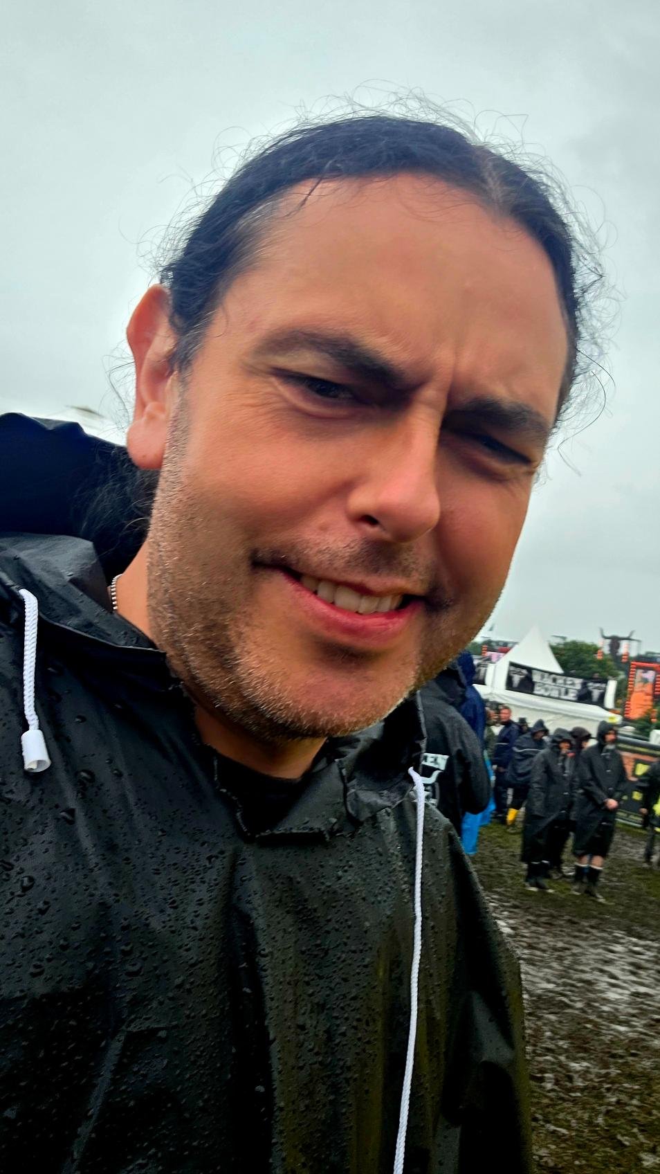 Xavi at Wacken Open Air 2025, smiling in a black rain poncho in muddy festival grounds