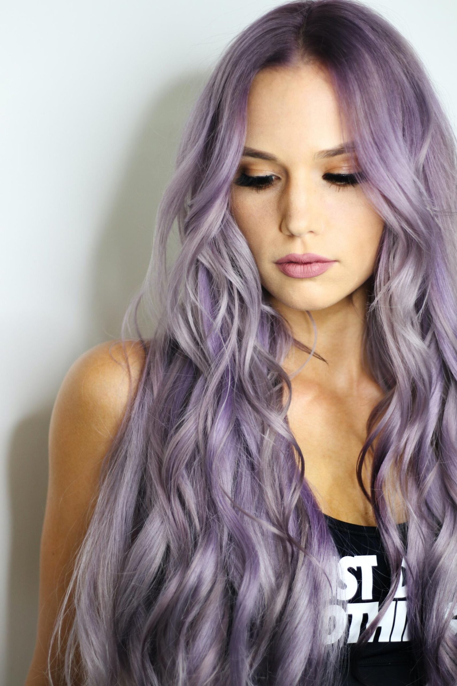Woman with long lavender wavy hair looking down against plain background.