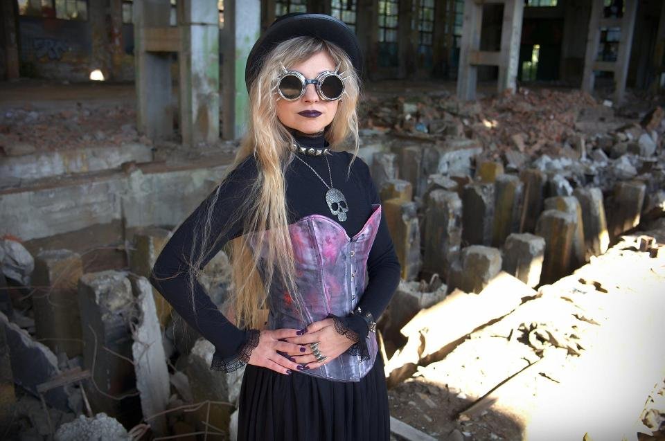 Gothic woman in corset and skull pendant standing in abandoned building.