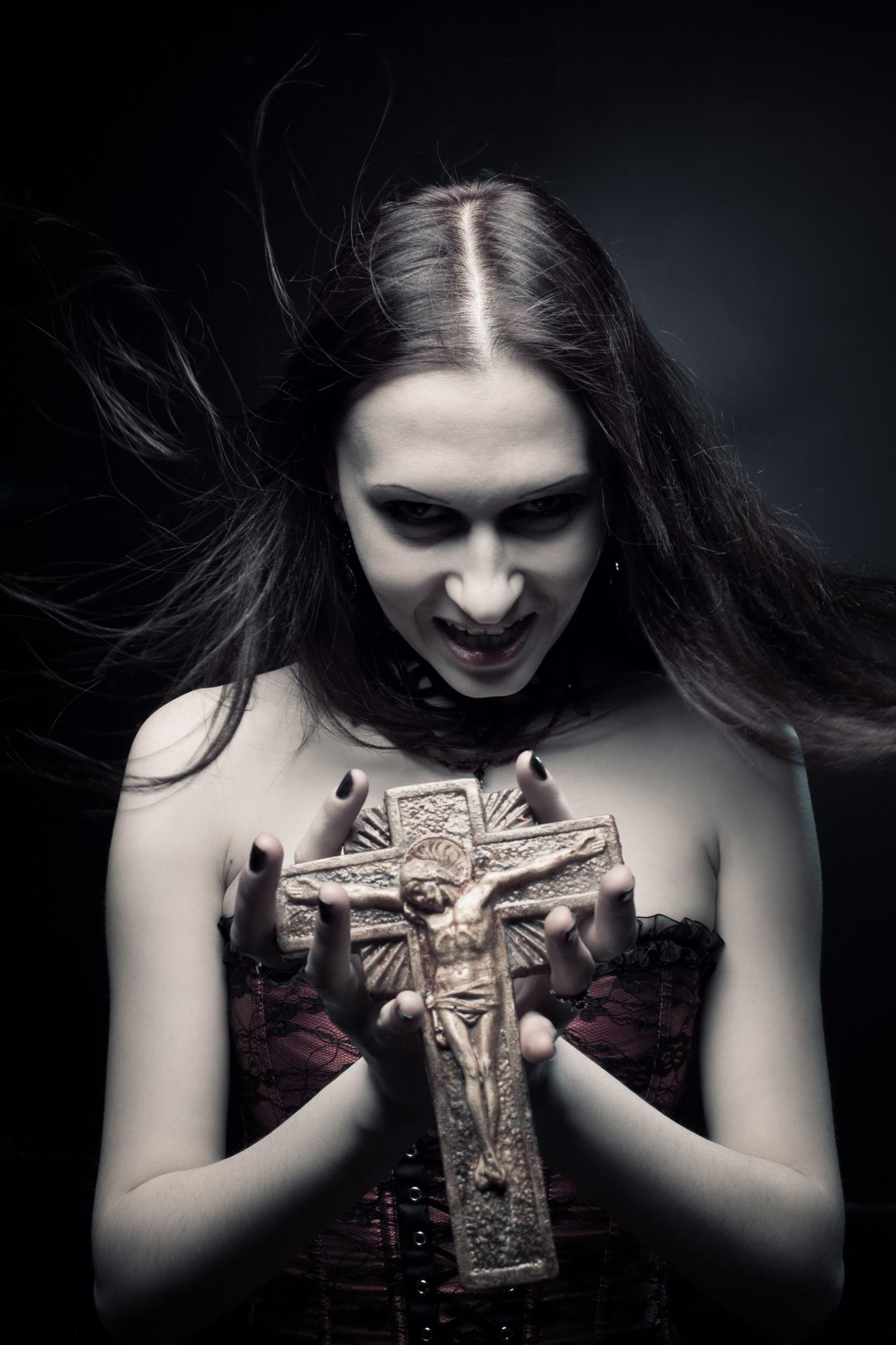 Gothic woman with long dark hair in a red corset, holding a large crucifix with a sinister expression. 