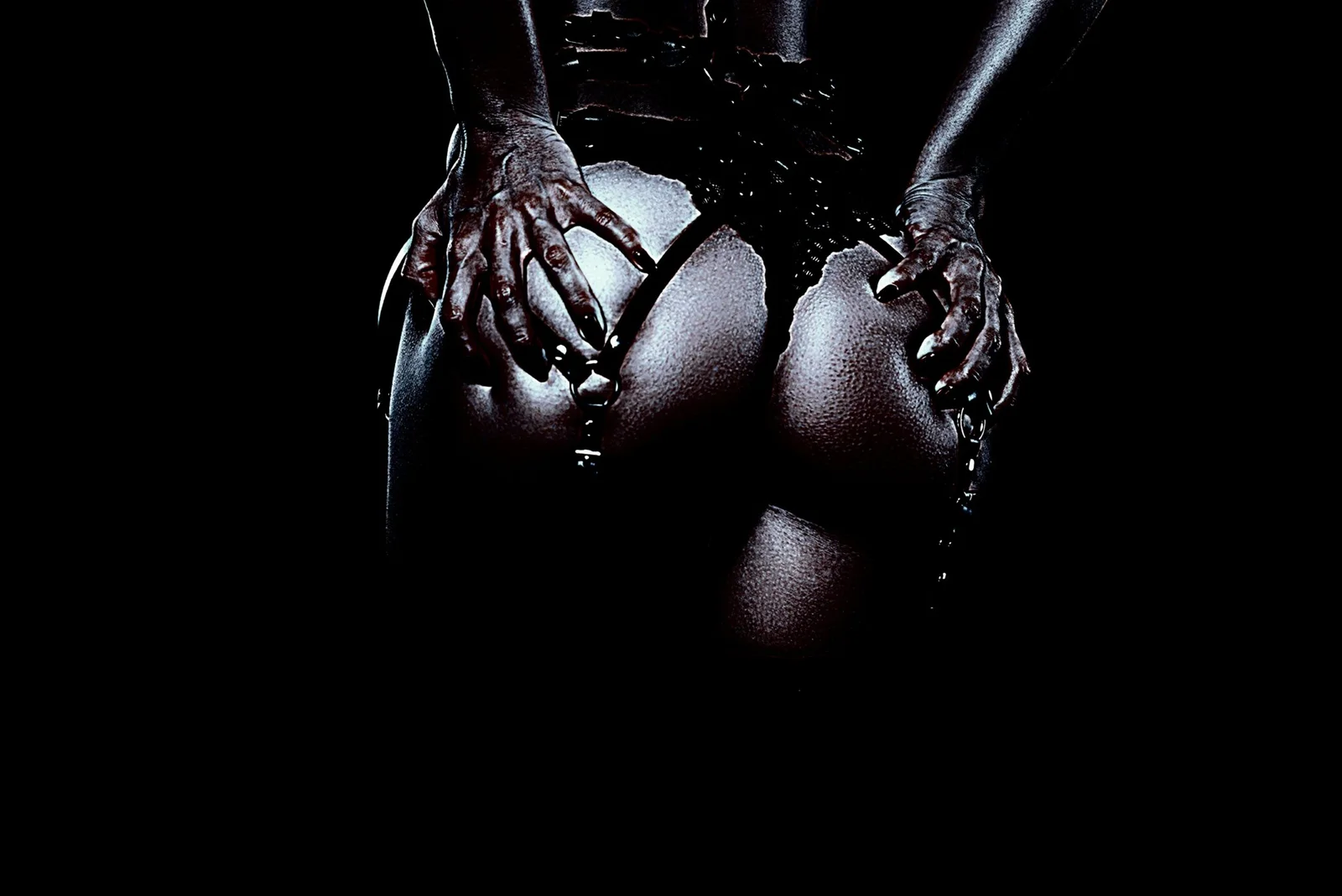 Close-up of hands gripping thighs in dark gothic lingerie, dramatic lighting against black background.