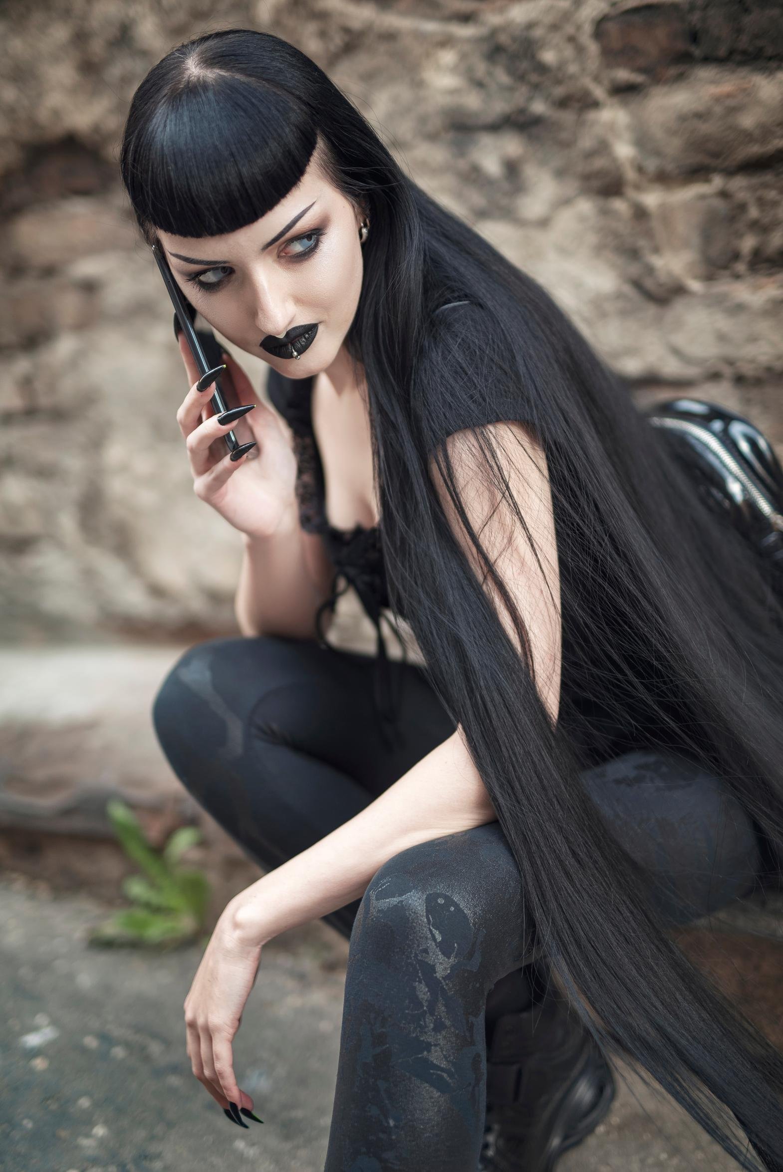 Close-up of gothic woman with black lipstick and long nails holding a phone
