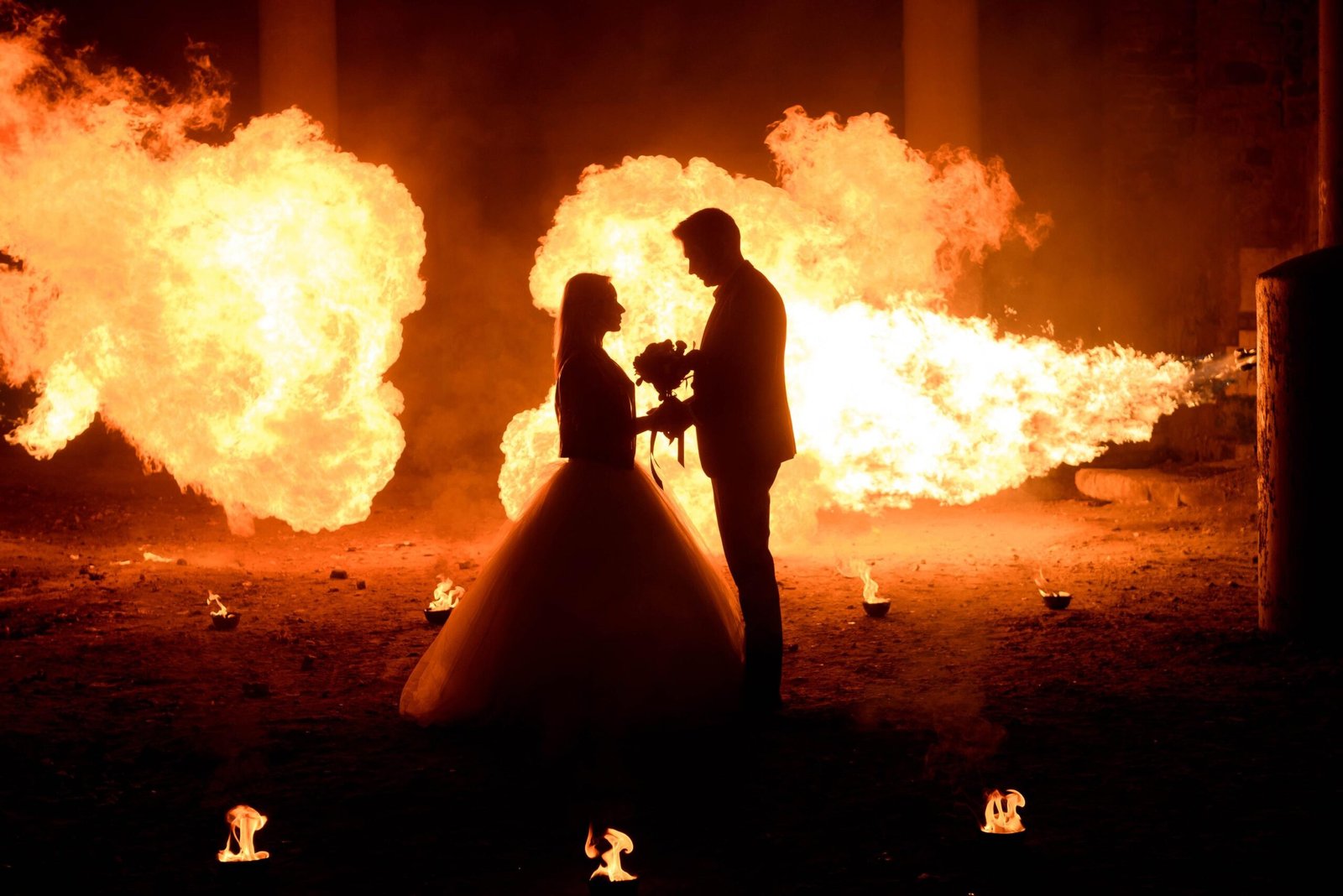 Silhouette couple holding hands in front of fire and explosions at night.