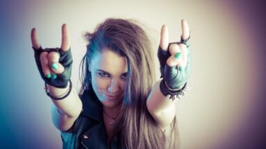 Metalhead woman smiling with leather vest and spiked bracelet making devil horns hand sign