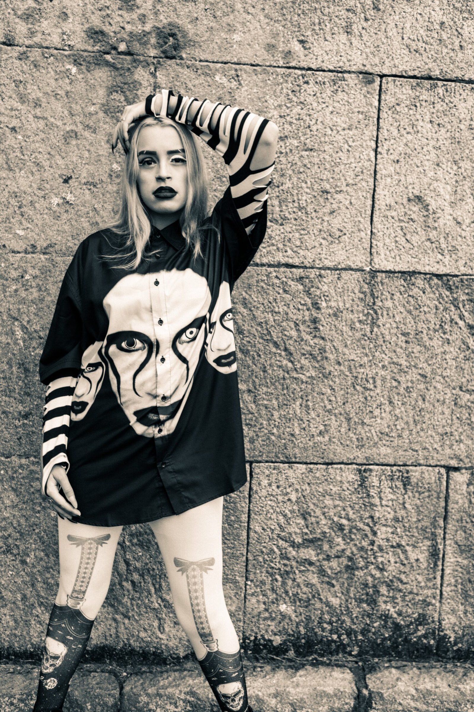 Urban goth woman in skull-print tights and oversized striped shirt, alternative street style with edgy attitude.