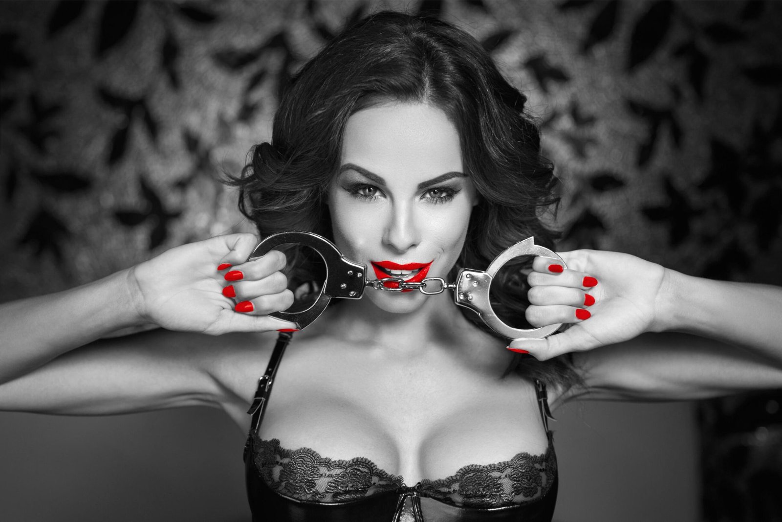 Black and white portrait of woman with red lips and nails holding handcuffs