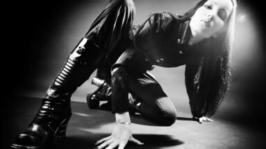 Gothic woman in black leather boots and outfit posing dramatically on floor under moody lighting.