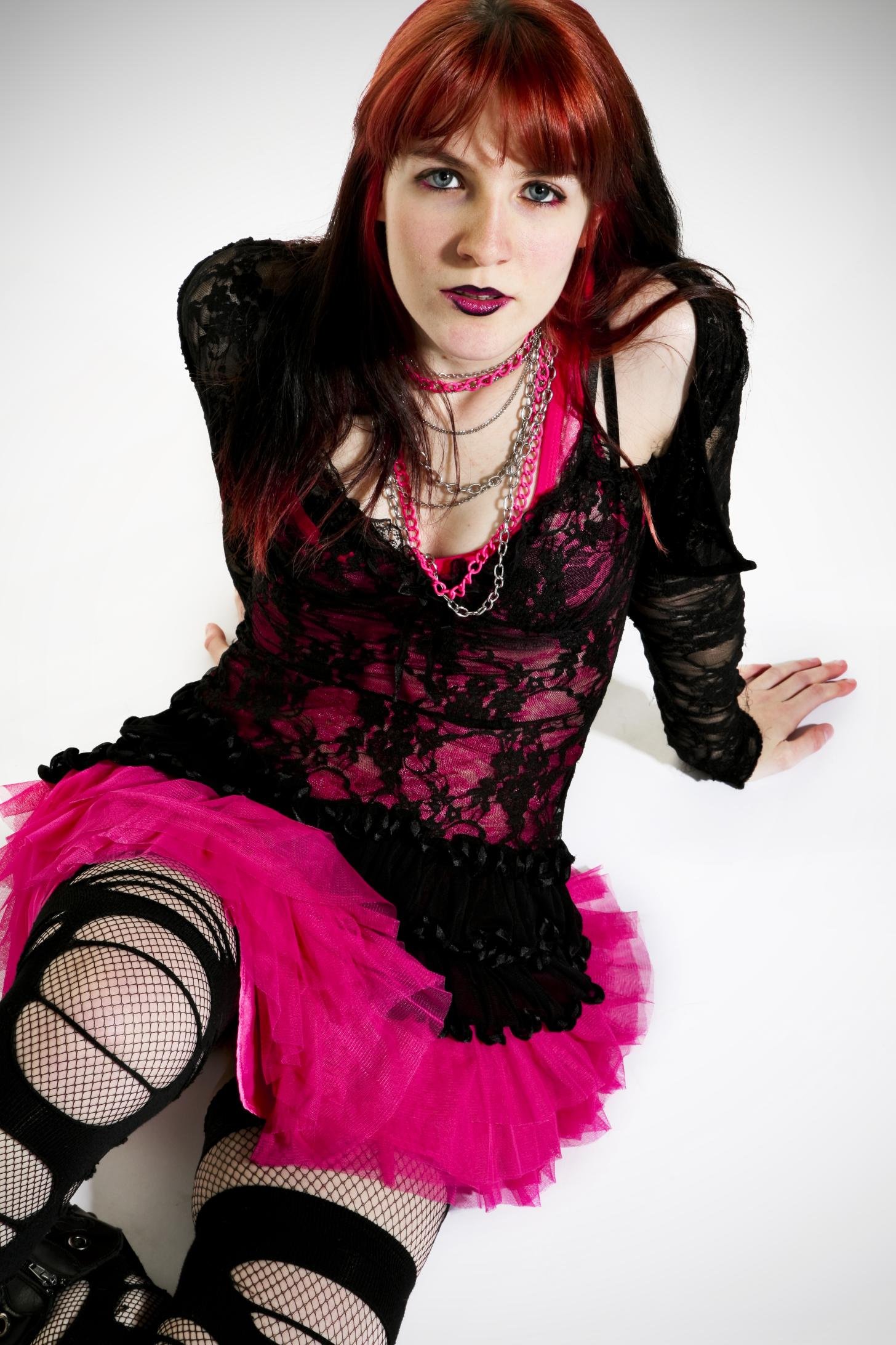 Alternative goth woman wearing pink and black lace skirt and fishnet stockings sitting on floor.