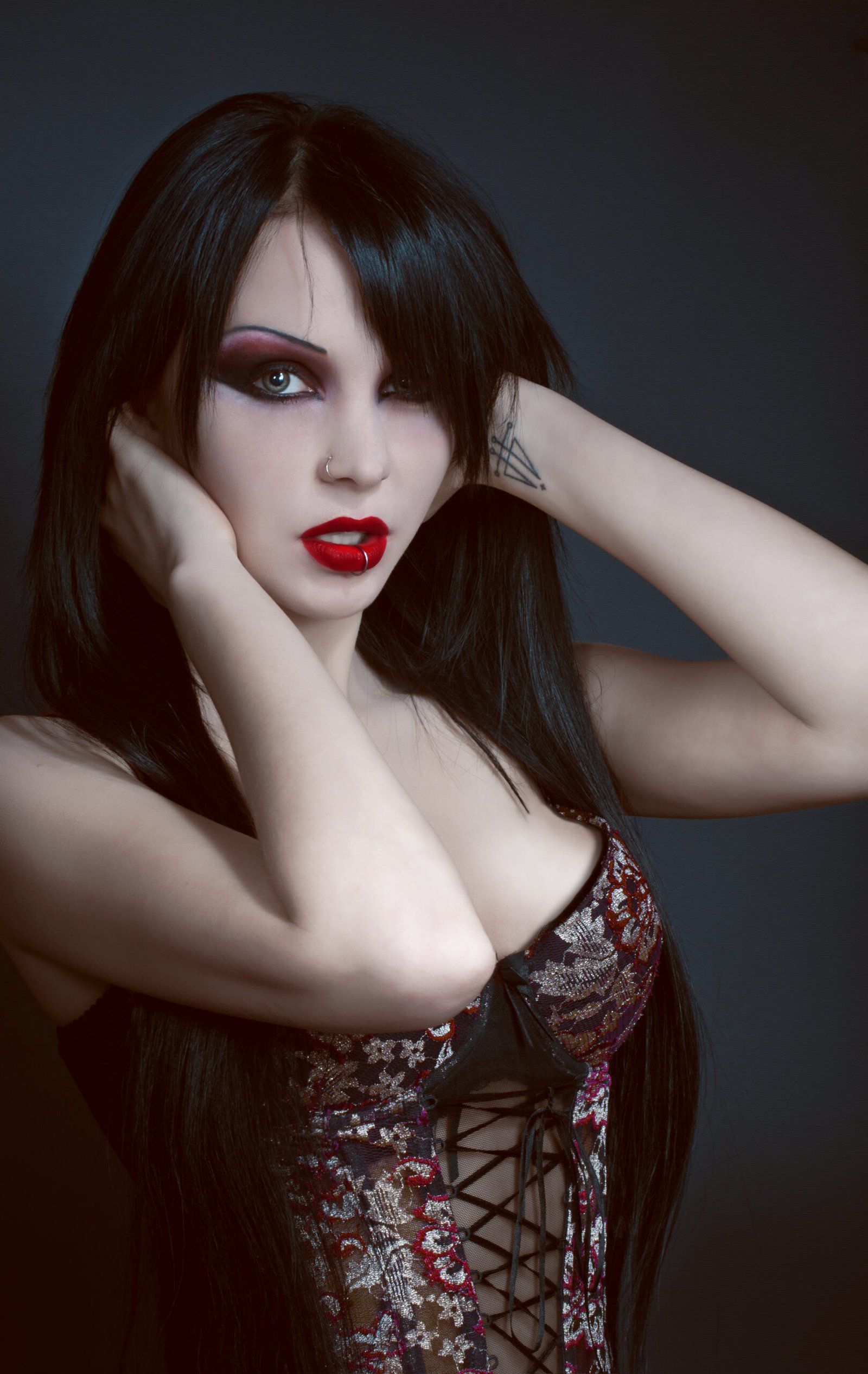 Goth woman with black hair, red lips, and smoky eye makeup holding her head with her hands.
