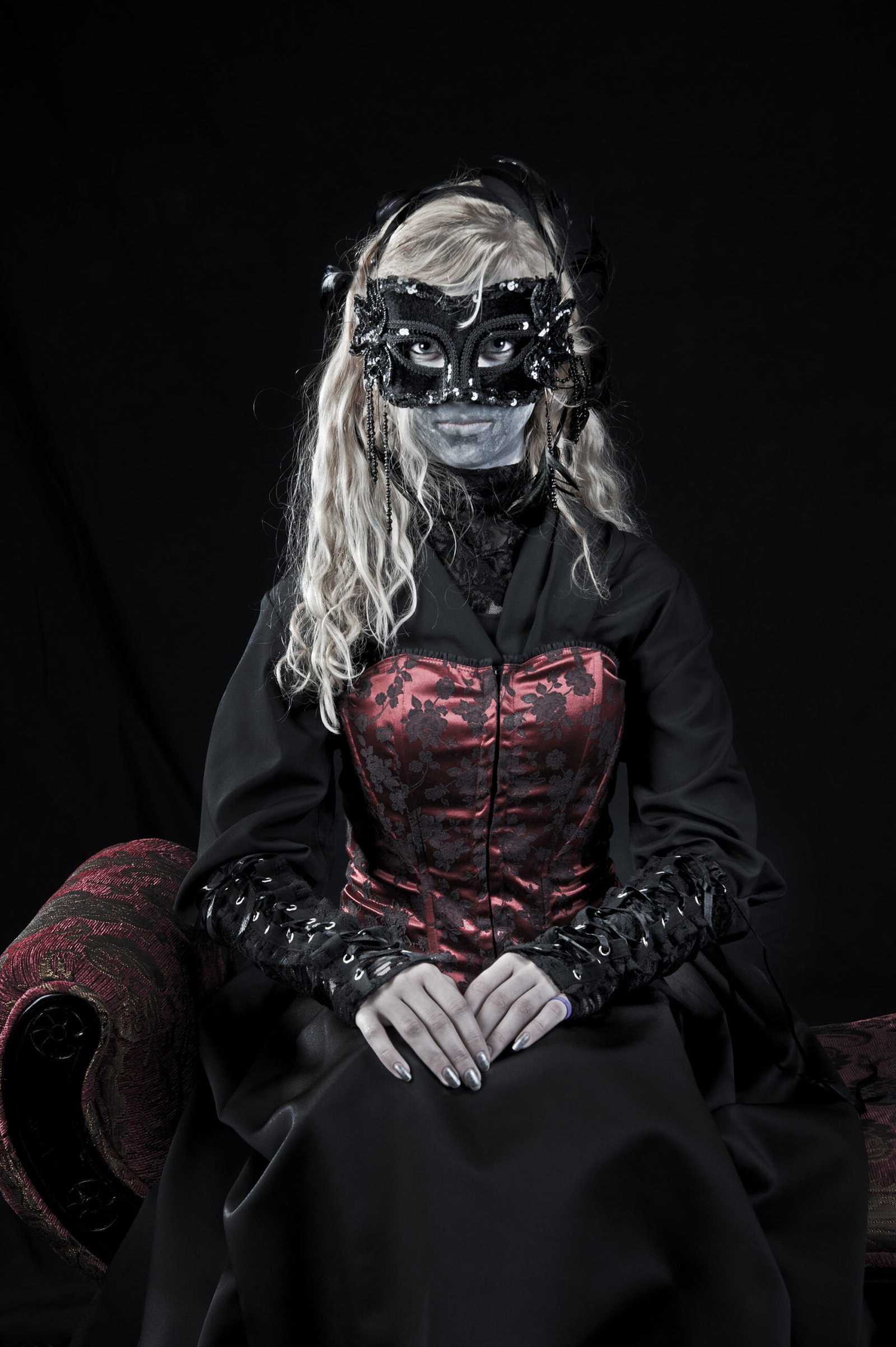 Goth woman in Victorian mask and corset, dark elegance, gothic fashion with dramatic black-and-red contrast.