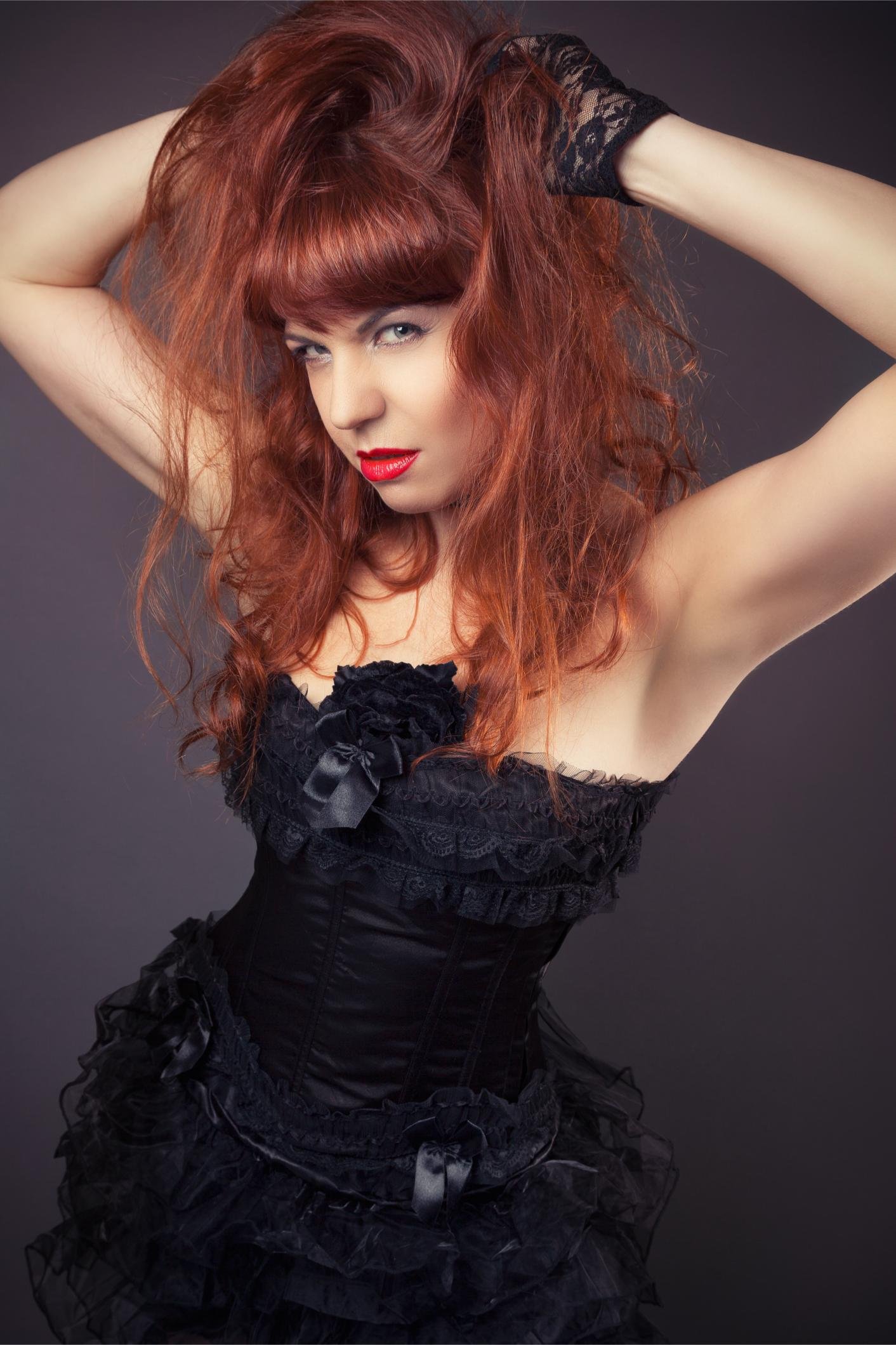 Woman with messy red hair wearing a black lace gothic corset and ruffled skirt.
