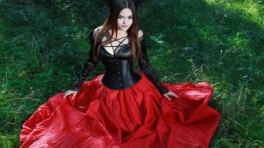 Gothic woman in a black corset and red skirt posing in a forest clearing.