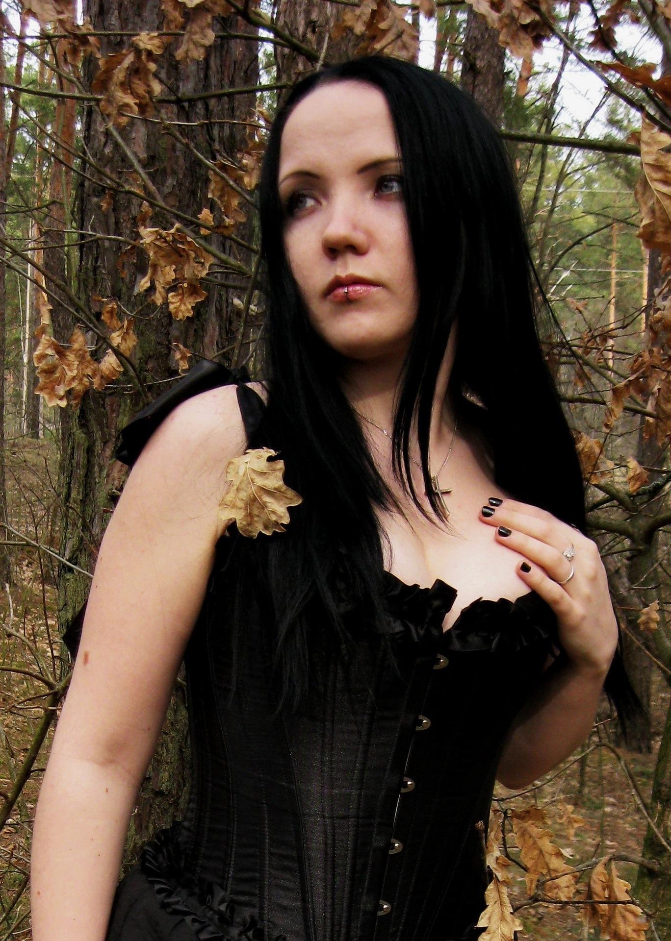 Woman with long black hair in a black corset standing among autumn trees in a forest.