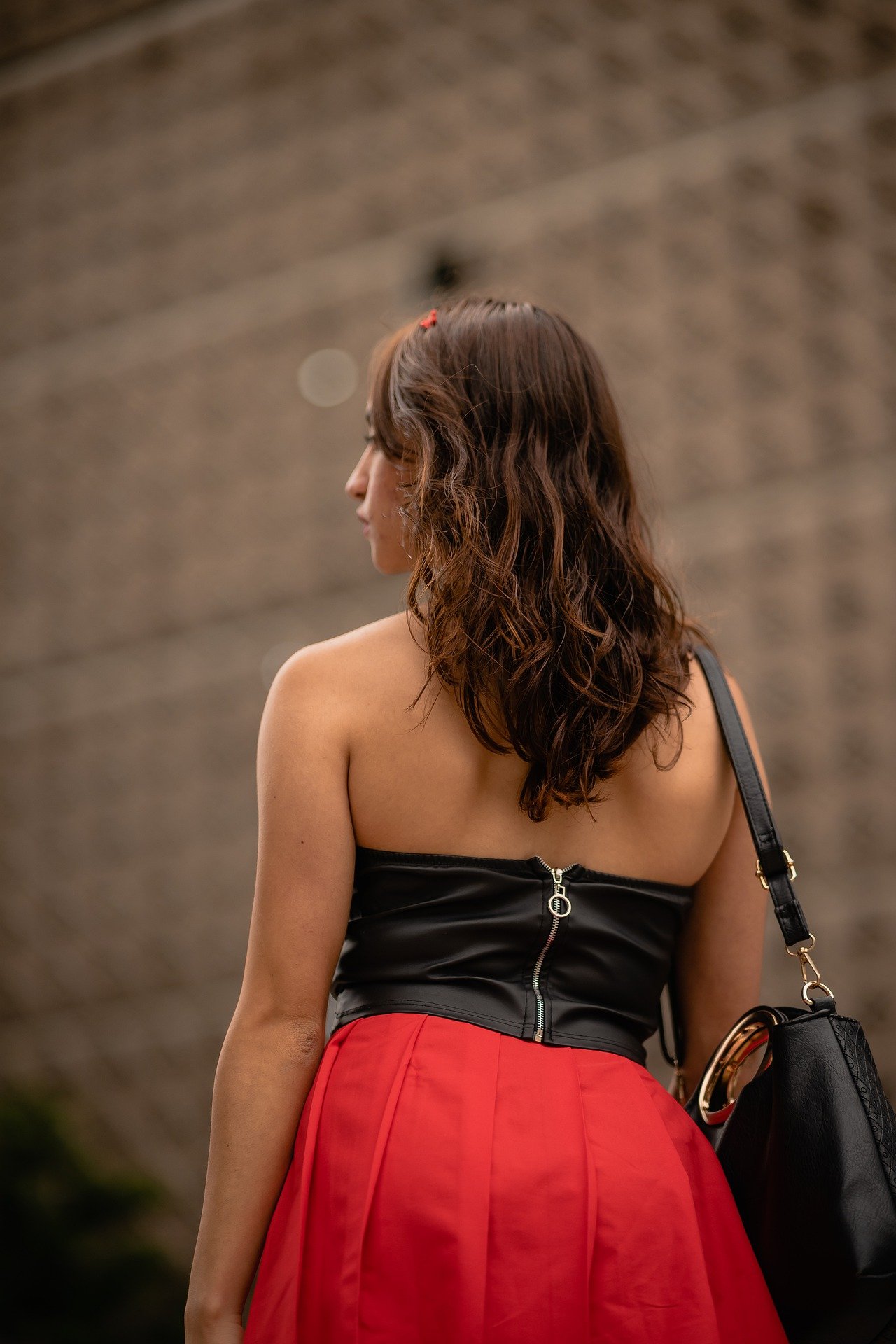 Woman viewed from behind wearing a black strapless top and red skirt, carrying a handbag outdoors