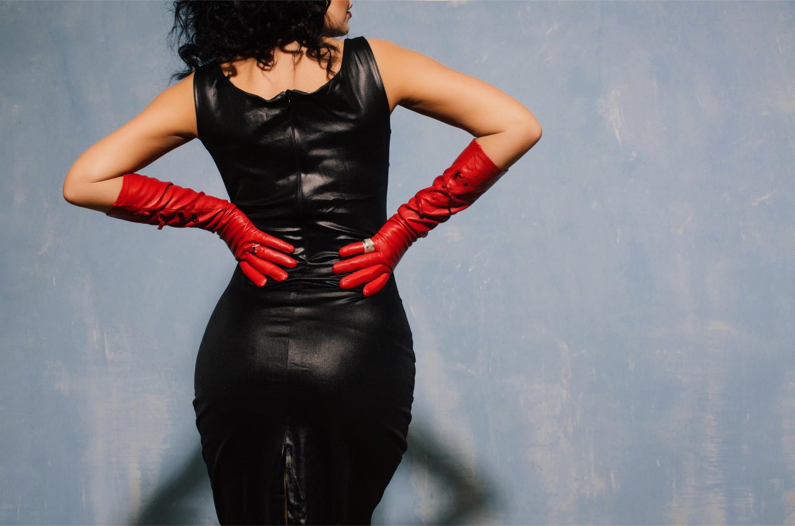 Back view of woman in black leather dress wearing long red gloves.