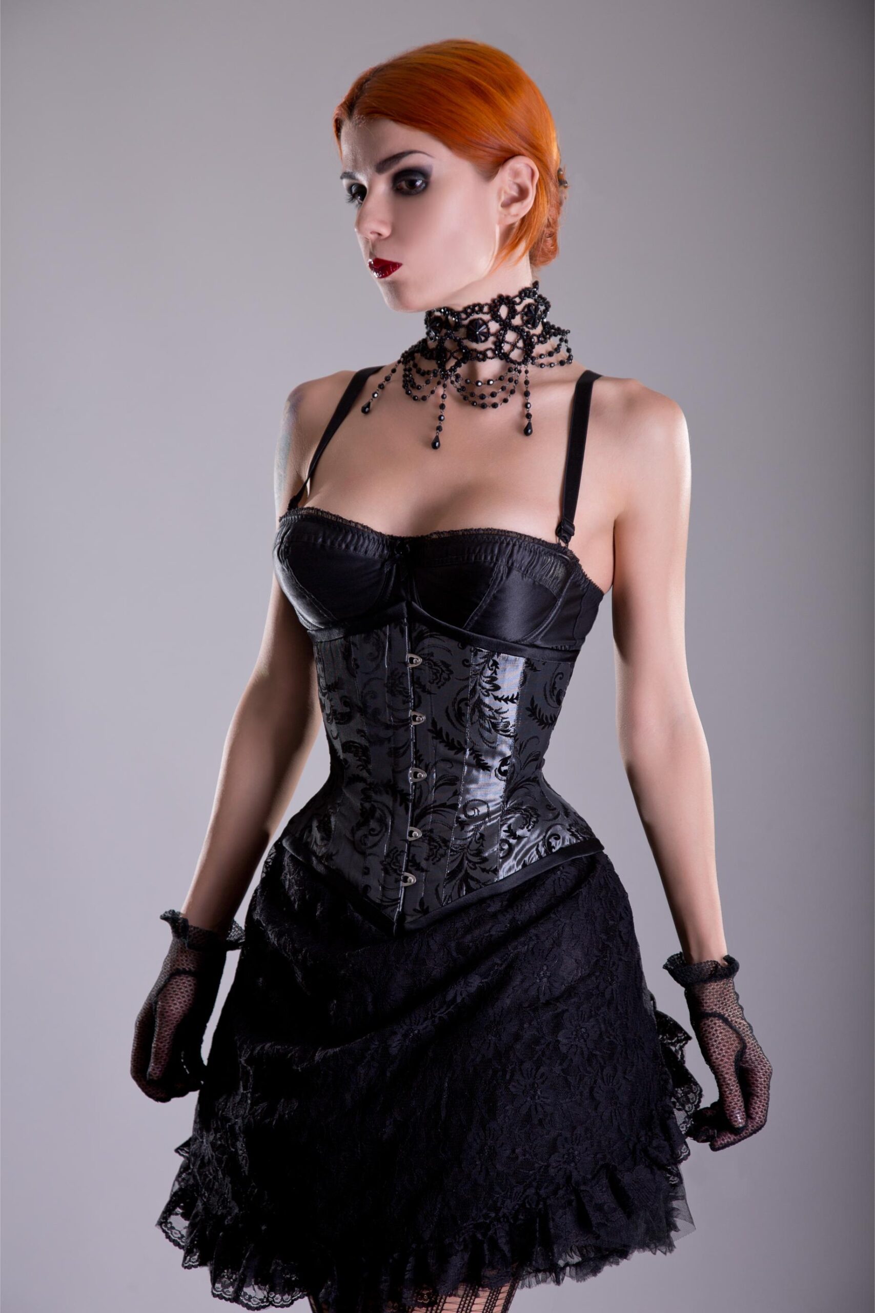 Woman with short orange hair wearing black corset and lace skirt with gothic choker.