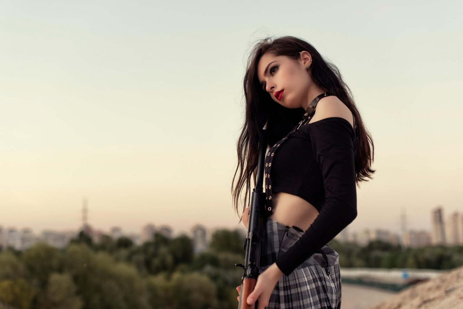 Woman in black crop top holding rifle against city skyline at sunset.