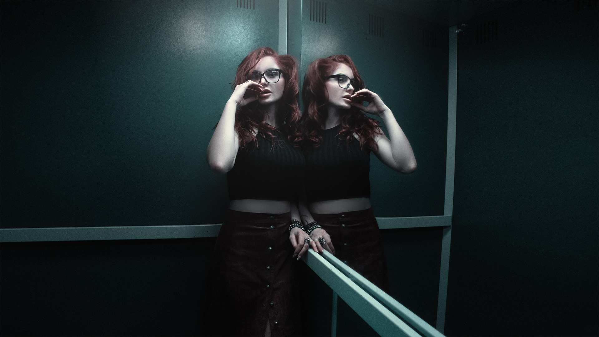 Red-haired woman with glasses standing in elevator beside mirror reflection.