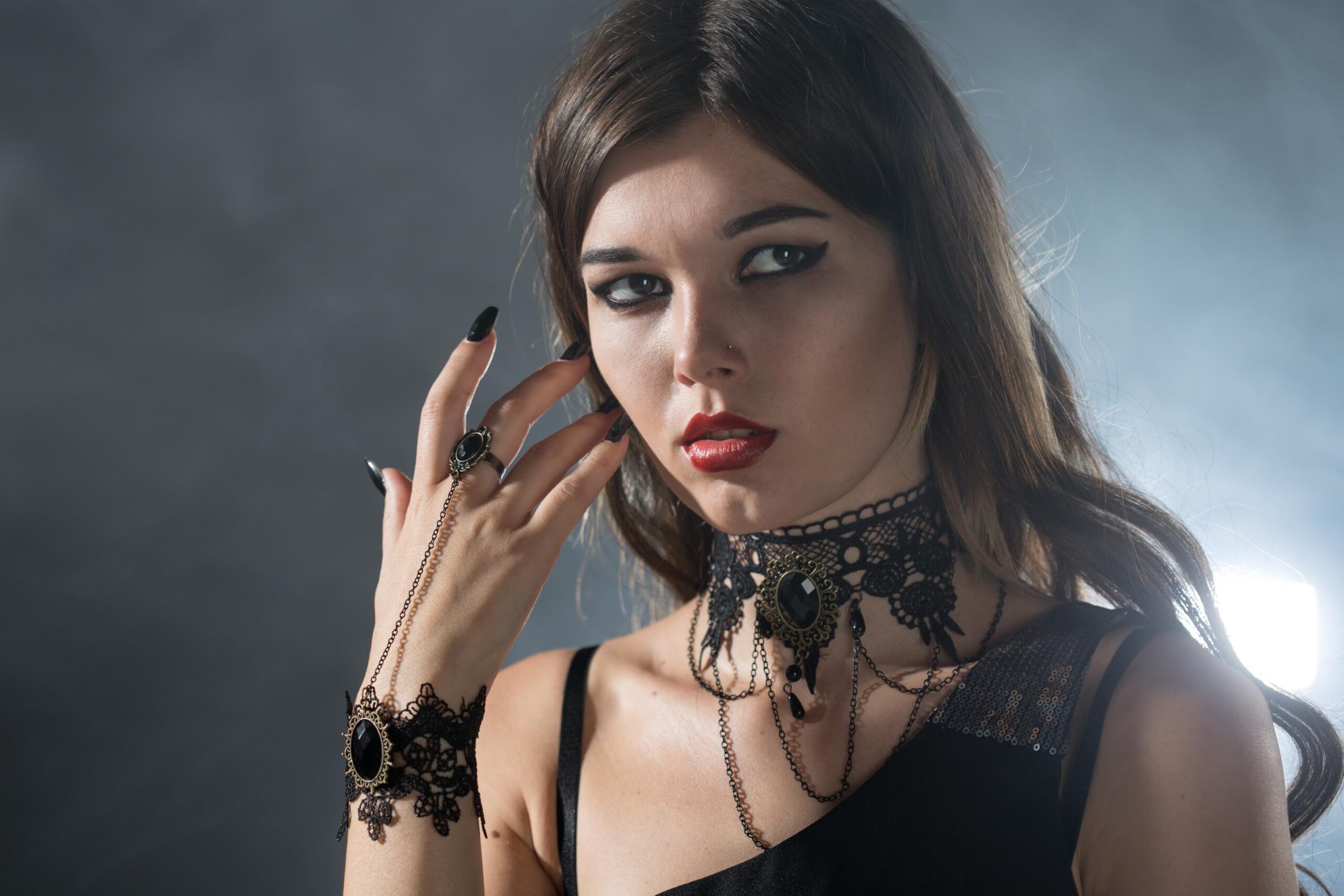 Close portrait of woman with gothic jewelry, lace choker and bracelet, dramatic makeup and red lipstick.