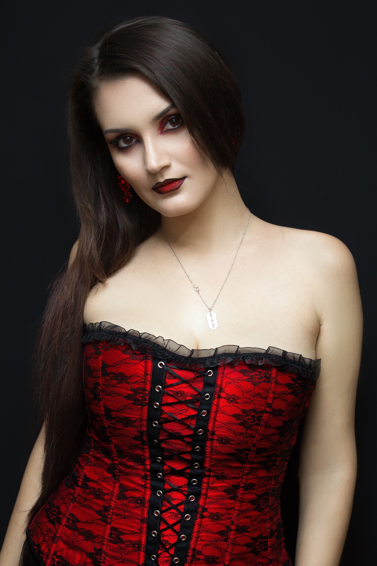 Portrait of woman in red lace corset with dark makeup against black background.
